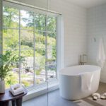 Serene bathroom with a freestanding tub, large picture window, and white tiled walls.