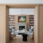 Modern library with stone fireplace, built-in bookshelves, and cozy midcentury-inspired seating.