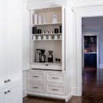 Built-in coffee bar with white cabinetry, marble countertop, and shelves for mugs and accessories