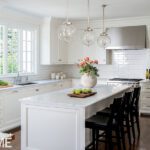 Bright white kitchen with glass globe pendant lights, marble island, and classic cabinetry