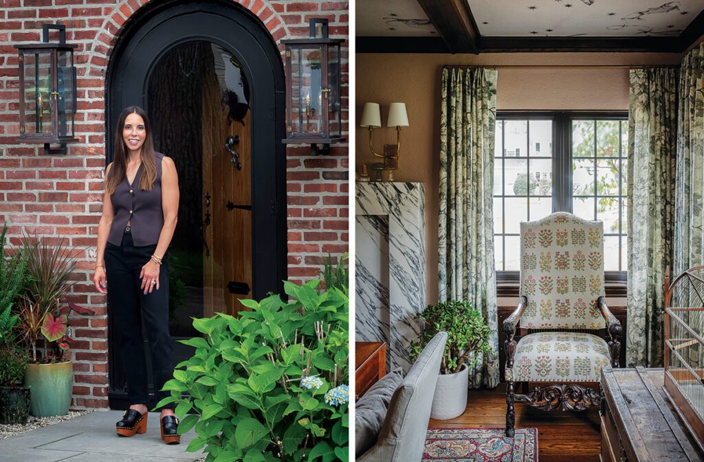 Interior designer Noelani Zervas stands at the entrance of a red brick home with black arched door and Antique carved wood chair with floral upholstery in a traditional sitting room with marble fireplace and patterned drapery