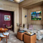 Sophisticated den with a taupe velvet sofa, cube ottomans, and colorful framed art on wood-paneled walls.