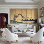 Serene living room with ivory furniture and a gilded Japanese screen depicting a cherry tree and ocean waves.