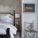 Bedroom corner with a black four-poster bed, textured wallpaper, and bronze sculptural chair.
