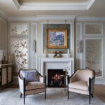 Elegant sitting area with two beige armchairs, a white fireplace, and decorative chinoiserie wall panels.