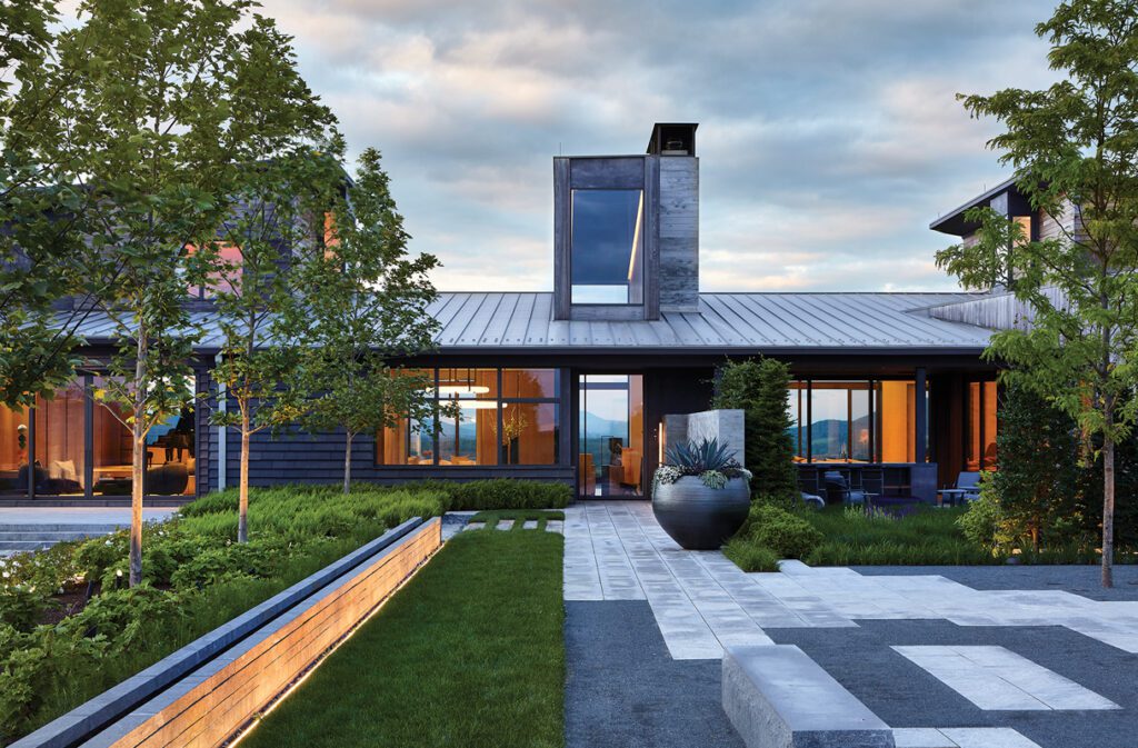 Modern home exterior with sleek metal roof, expansive windows, and lush landscaping at sunset.