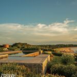 Sleek infinity pool with stone surround overlooking a sandy beach and ocean at sunset.