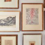 Eclectic gallery wall with framed sketches, etchings, and prints in gold frames.