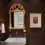 Elegant powder room with deep brown walls, gilded mirror, and framed geometric artwork.