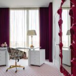 Modern white desk with floral chair, magenta drapery, and oversized mirror.