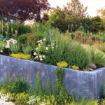 Raised concrete planter filled with colorful summer blooms, grasses, and textured greenery.