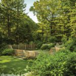 Elegant tennis court enclosed by wooden lattice fencing, surrounded by mature trees and landscaped gardens.