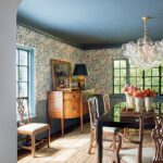 Formal dining room with patterned wallpaper, glossy blue ceiling, and modern chandelier