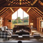 Cozy loft with exposed beams, plaid armchairs, and large window framing a countryside view.