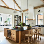 Open kitchen with wood beams, black countertops, large island, and glass-front cabinets.
