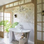 Freestanding bathtub with sculptural side table, botanical wallpaper, and natural wood trim.