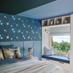 Space-themed boys’ bedroom with celestial wallpaper, blue ceiling, and built-in window seat.
