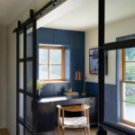 Home office nook with navy paneling, wood desk, and glass sliding doors.