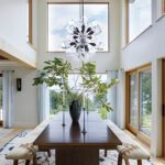 Dining room with tall windows, wooden table, and sculptural chandelier.