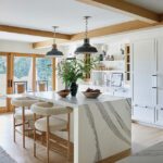 White kitchen with marble waterfall island, pendant lights, and wood beams.