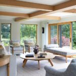 Bright living room with wood ceiling beams, neutral furnishings, and large windows overlooking the garden.