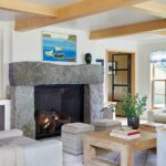Living room with rustic stone fireplace, wood beams, and coastal artwork.