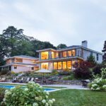 Modern home exterior with large windows, landscaped garden, and poolside patio.