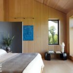 Minimalist bedroom with wood-paneled walls, contemporary artwork, and expansive windows.
