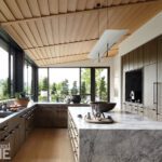 This expansive kitchen balances luxury and functionality with marble surfaces, modern lighting, and a wraparound view of verdant outdoor spaces.