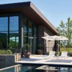 Modern poolside terrace with lounge chairs, umbrellas, and glass-walled exterior.