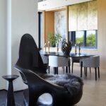 Organic modern chair with fur throw beside a sleek dining table and gold-toned accents.