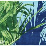 Handwoven rug in shades of blue and green featuring abstract tropical leaf and shadow patterns.