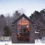 Contemporary barn-inspired home with expansive glass facade glowing warmly in a snowy New England landscape.