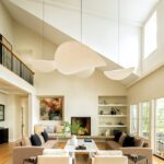 Sophisticated great room with sculptural pendant lights, neutral furniture, and high vaulted ceilings.