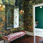 Scenic mural wallpaper in a hallway with pink patterned bench and brass wall sconces