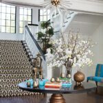 Grand entryway with round pedestal table, floral arrangement, and staircase with patterned runner