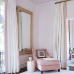 Soft pink bedroom seating area with chaise lounge, oversized mirror, and white drapery