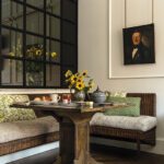 Banquette dining nook with wicker seating, pedestal table, and vintage portrait.
