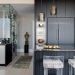 Glass-enclosed wine storage beside modern kitchen island with pendant lighting.