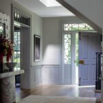 Elegant entryway with paneled walls, skylight, and classic glass-paneled front door.