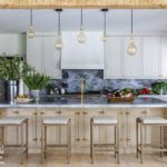 Modern farmhouse kitchen with marble island, pendant lights, and light wood cabinetry.
