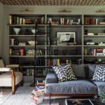 Home library with built-in shelving, rolling ladder, and gray sofa.