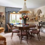 Traditional dining room with scenic wall mural, round wood table, and patterned chairs.