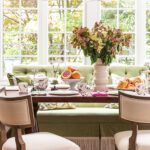 Bright breakfast nook with green banquette seating, wood table, and floral arrangement.