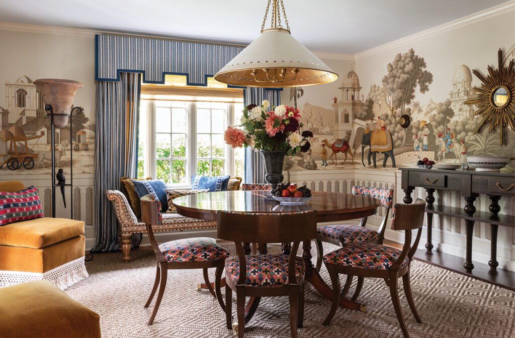 Traditional dining room with scenic wall mural, round wood table, and patterned chairs.