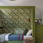 Children’s bedroom with green alcove bed, woodland wallpaper, and built-in drawers.