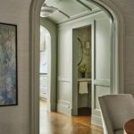 View through arched doorway into powder room with green paneled walls, round mirror, and marble vanity.