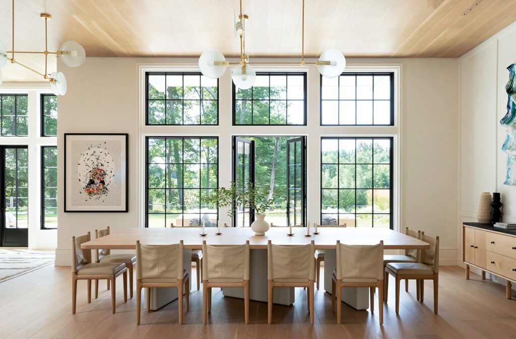 Light-filled great room with grand piano, modern chandeliers, and large windows connecting the interior to the outdoors.