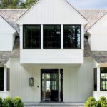 Modern farmhouse exterior with white vertical siding, gabled roof, and black-framed windows at the front entry.