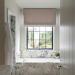 Luxurious bathroom with marble tub surround, windowed view, and modern brass light fixture above.